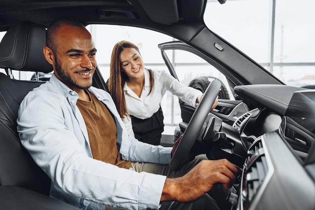 Young attractive woman salesperson in car showroom showing a car to her client