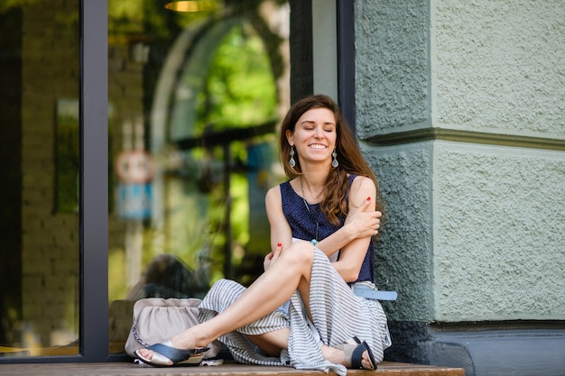 Young attractive woman sits crosslegged by a huge window outdoors