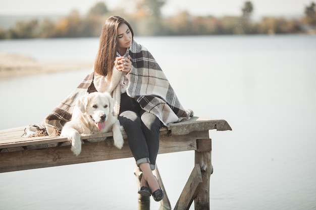 彼女の犬と一緒に桟橋に座っている若い魅力的な女性。屋外の親友