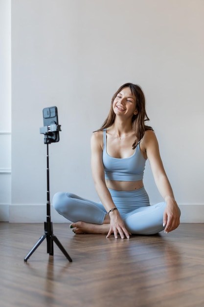 Foto giovane donna attraente seduta sul pavimento durante la lezione di yoga mentre si utilizza lo smartphone prima dell'allenamento