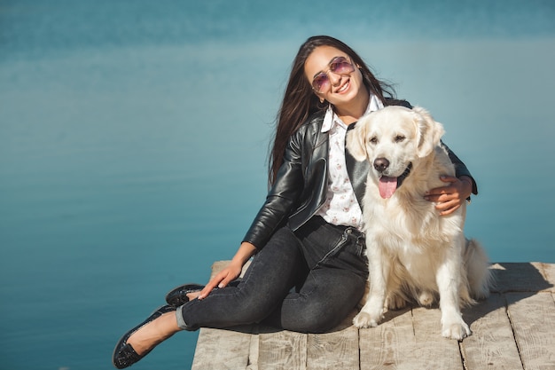 彼女の犬と桟橋に座っている若い魅力的な女性。屋外の親友