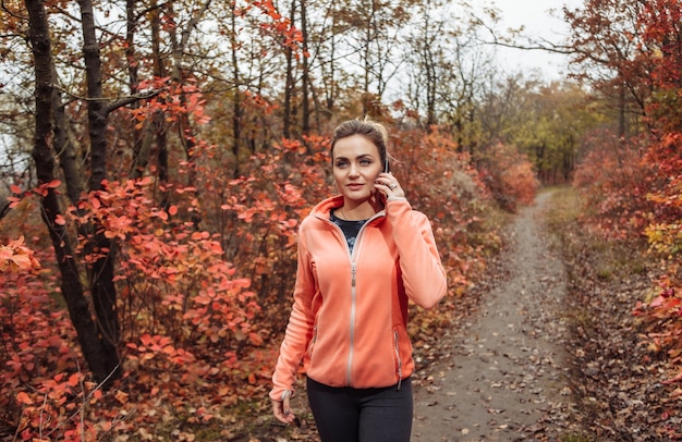 Молодая привлекательная женщина в спортивной одежде разговаривает по телефону во время прогулки по тропе