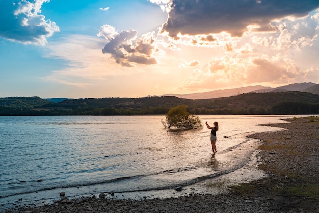 Молодая привлекательная женщина фотографируется в красивом озере летом во время путешествия на закате