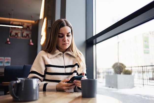 Giovane donna attraente che parla su un telefono cellulare e sorride mentre è seduto da solo in un caffè nel suo tempo libero e lavora la donna felice sta riposando in un caffè stile di vita