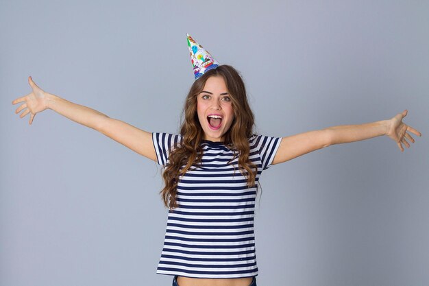 Молодая привлекательная женщина в раздетой футболке и праздничной кепке на сером фоне в студии