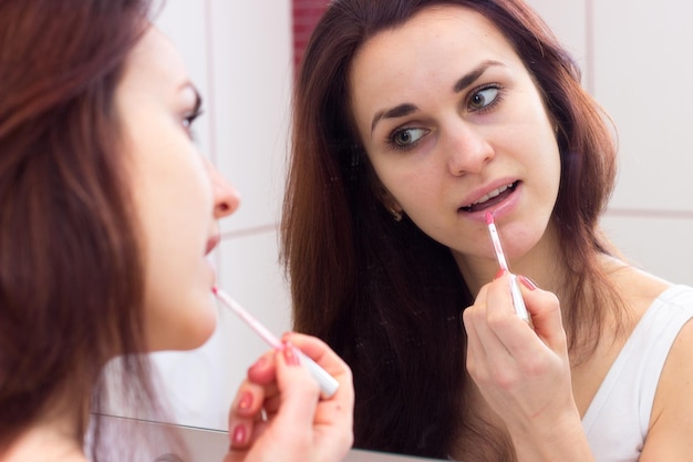 그녀의 버건디 욕실에서 거울 앞에서 광택 흰색 셔츠 립글로스에 젊은 매력적인 여자