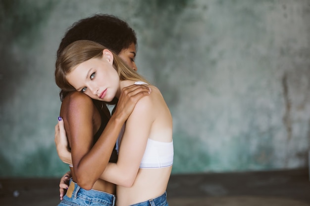 Giovane donna attraente con capelli biondi in cima che abbraccia la ragazza afroamericana mentre pensieroso