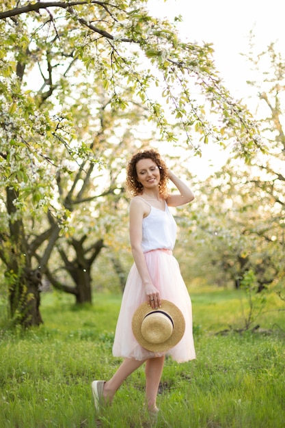 Young attractive woman with curly hair walking in a green flowered garden. Spring mood