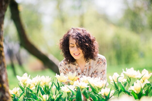 Young attractive woman with curly long hair posing in spring blooming garden, apple trees