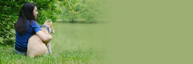 Young attractive woman with dark long hair sits on the shore of a pond hugging a dog