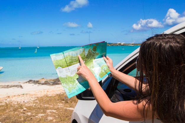 Giovane donna attraente con la grande mappa dell'isola in macchina
