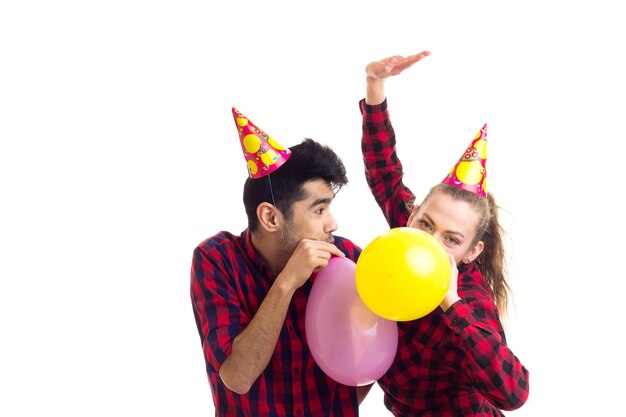 Young attractive woman with handsome man in plaid shirts with celebrating hats blowing balloons