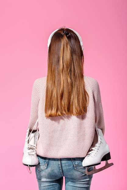 Young attractive woman with ice skates stands with back