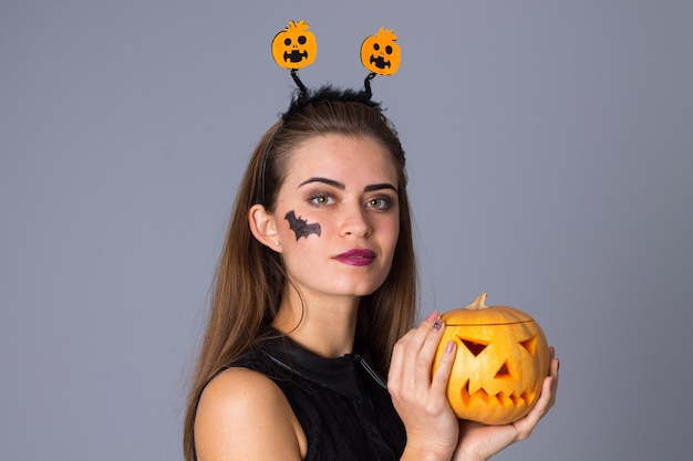 Young attractive woman with pumpkins in black dress holding a pumpkin on blue background in studio