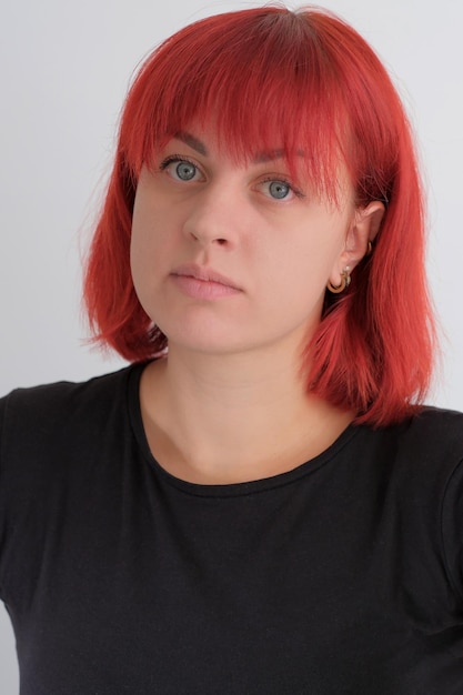 A young attractive woman with a short orange hairstyle in a black Tshirt and jeans posing in the studio on a white background