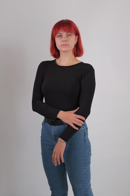 A young attractive woman with a short orange hairstyle in a black Tshirt and jeans posing in the studio on a white background