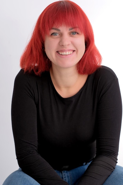 A young attractive woman with a short orange hairstyle in a black Tshirt and jeans posing in the studio on a white background