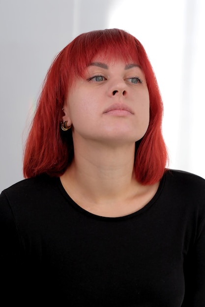 A young attractive woman with a short orange hairstyle in a black Tshirt and jeans posing in the studio on a white background