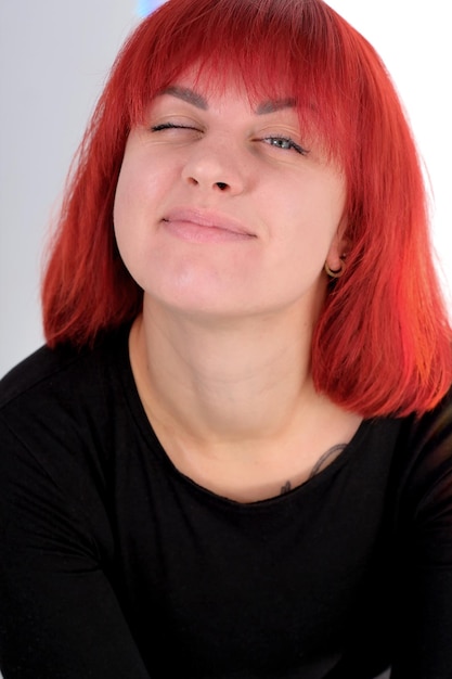 A young attractive woman with a short orange hairstyle in a black Tshirt and jeans posing in the studio on a white background