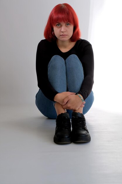 A young attractive woman with a short orange hairstyle in a black Tshirt and jeans posing in the studio on a white background