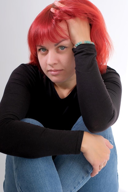 A young attractive woman with a short orange hairstyle in a black Tshirt and jeans posing in the studio on a white background