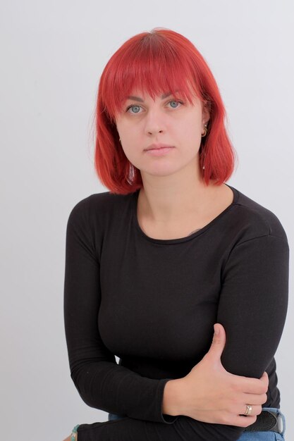 A young attractive woman with a short orange hairstyle in a black Tshirt and jeans posing in the studio on a white background