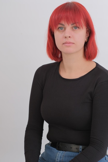 A young attractive woman with a short orange hairstyle in a black Tshirt and jeans posing in the studio on a white background