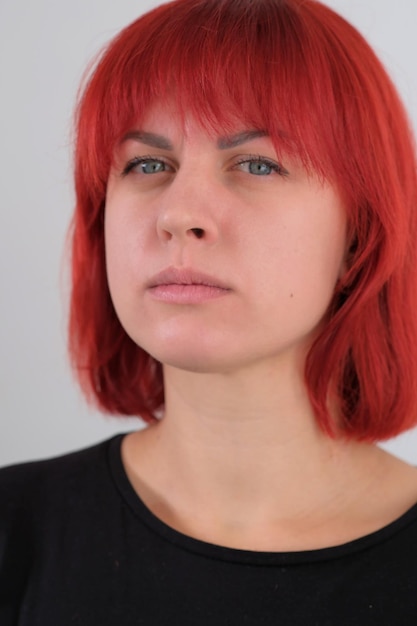 A young attractive woman with a short orange hairstyle in a black Tshirt and jeans posing in the studio on a white background