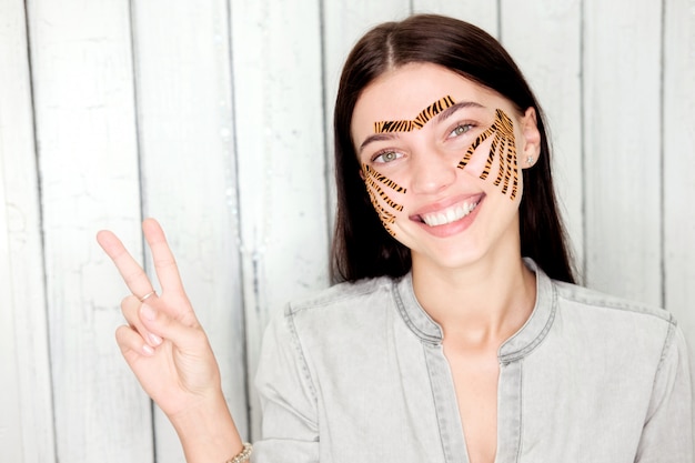 Young attractive woman with tiger colored tapes show "V" sign with fingers after taping face procedure in beauty parlor