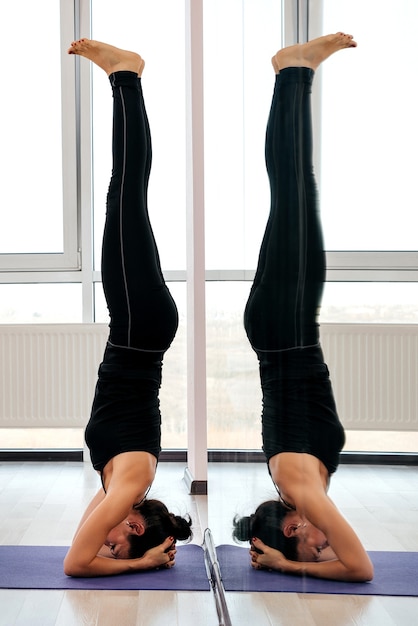 Giovane donna attraente yogi praticando il concetto di yoga, facendo headstand pongono, lavorando, indossando