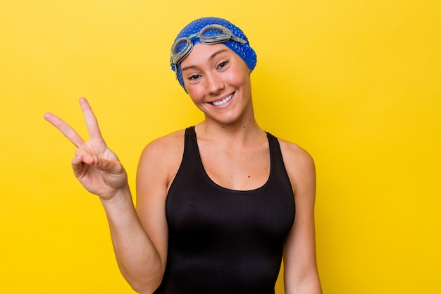 Young australian swimmer woman isolated on yellow background joyful and carefree showing a peace symbol with fingers.