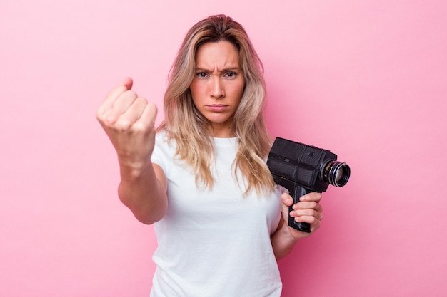 分離されたビンテージビデオカメラで撮影している若いオーストラリア人女性は、カメラに拳、攻撃的な表情を示しています。