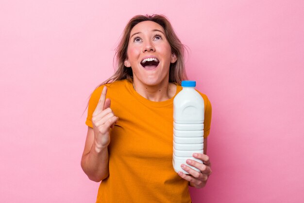 Young australian woman holding a bottle of milk isolated on pink background pointing upside with opened mouth.