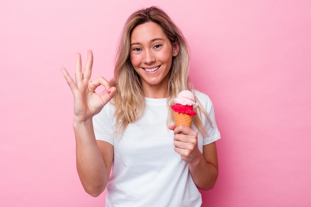 Young australian woman holding an ice cream isolated on pink background cheerful and confident showing ok gesture.