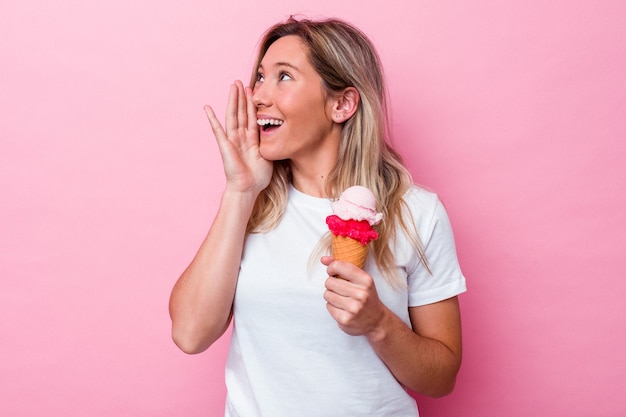 ピンクの背景に分離されたアイスクリームを持って叫び、開いた口の近くで手のひらを保持している若いオーストラリア人女性。