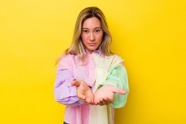 Young australian woman isolated holding something with palms, offering to camera.