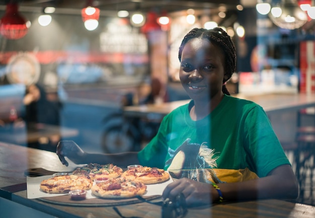 Молодая настоящая афроамериканка ест пиццу в ресторане ночного города
