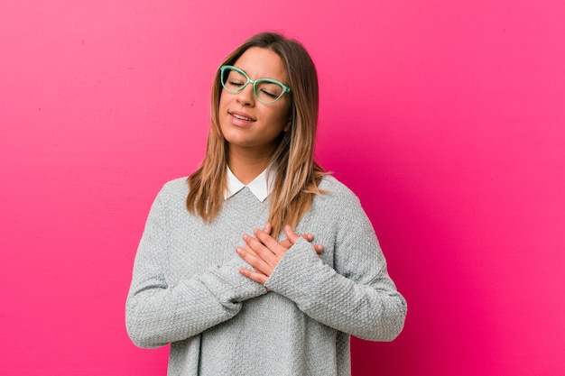 Young authentic charismatic real people woman against a wall has friendly expression, pressing palm to chest. Love concept.