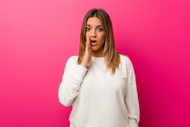 La giovane donna autentica carismatica della gente reale contro un muro sta dicendo una notizia di frenata calda segreta e sta guardando da parte