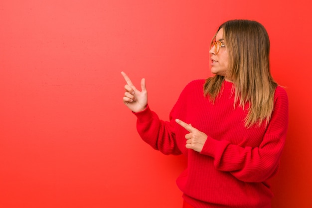 Young authentic charismatic real people woman against a wall shocked pointing with index fingers to a blank space.