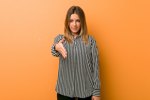 Young authentic charismatic real people woman against a wall stretching hand at camera in greeting gesture.