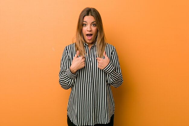 Young authentic charismatic real people woman against a wall surprised pointing with finger, smiling broadly.