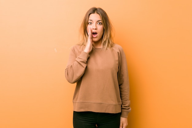 Young authentic charismatic  woman against a wall is saying a secret hot braking news and looking aside