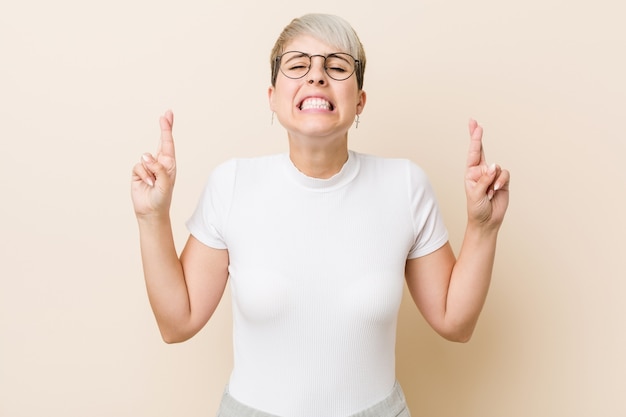 Young authentic natural woman wearing a white shirt crossing fingers for having luck