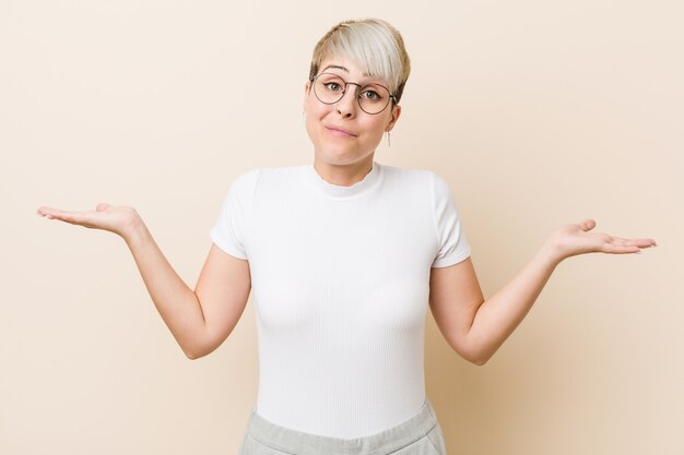 Young authentic natural woman wearing a white shirt doubting and shrugging shoulders in questioning gesture.