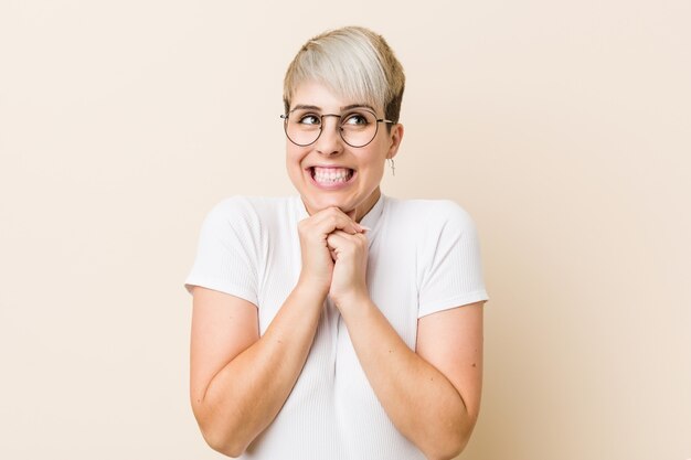 Young authentic natural woman wearing a white shirt keeps hands under chin, is looking happily aside.