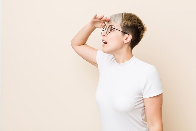 Young authentic natural woman wearing a white shirt looking far away keeping hand on forehead