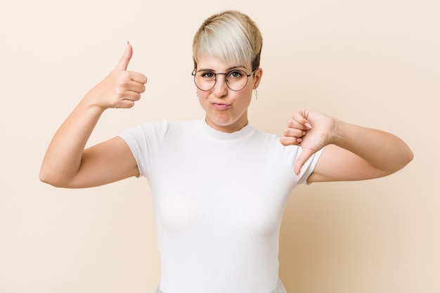 Giovane donna naturale autentica che indossa una camicia bianca che mostra i pollici in su e i pollici in giù