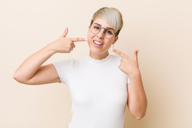 Young authentic natural woman wearing a white shirt smiles, pointing fingers at mouth.