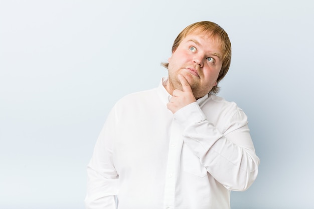 Young authentic redhead fat man looking sideways with doubtful and skeptical expression.